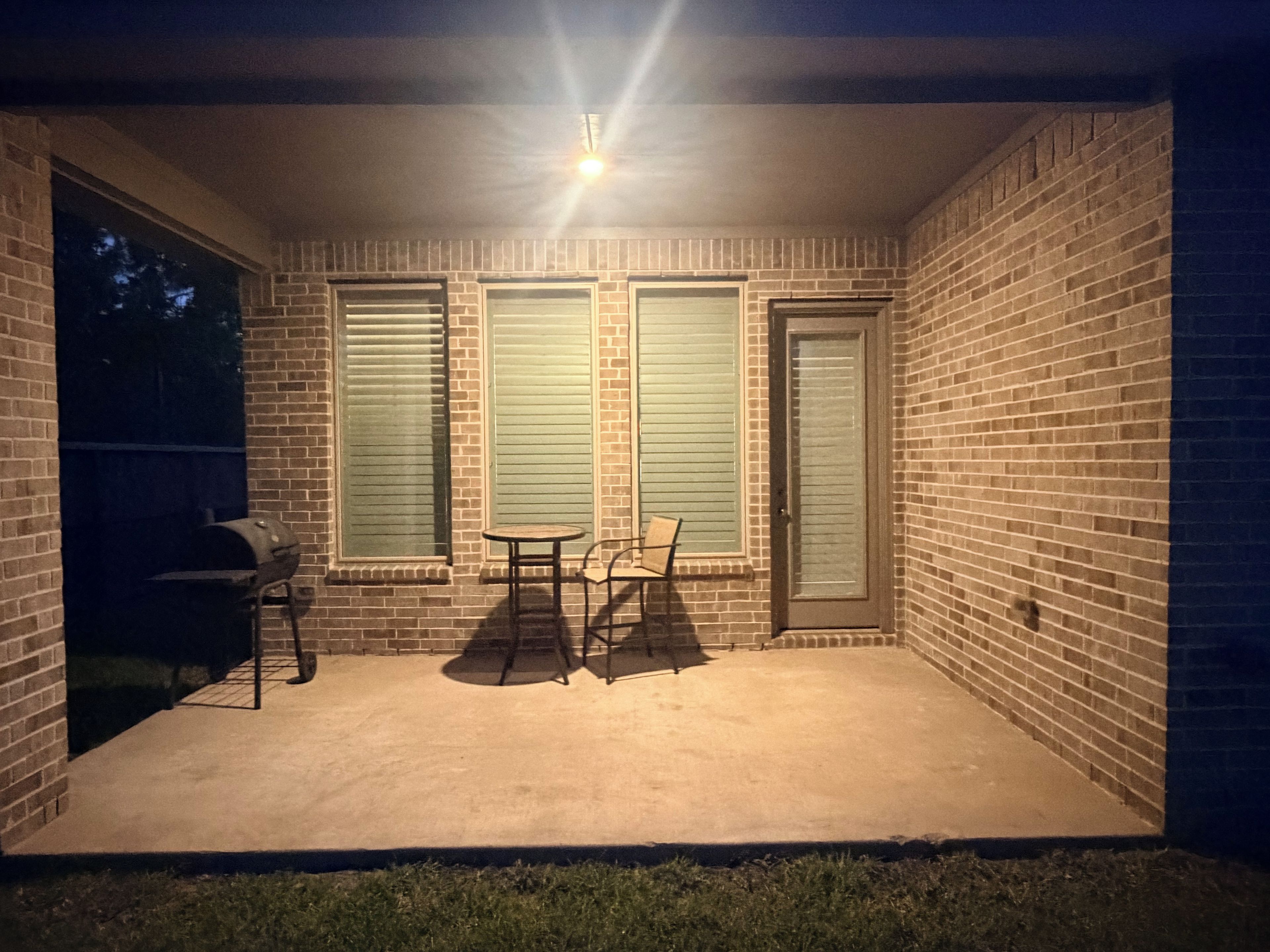 Ein überdachter Patio-Bereich mit Grill, Tisch und zwei Stühlen.