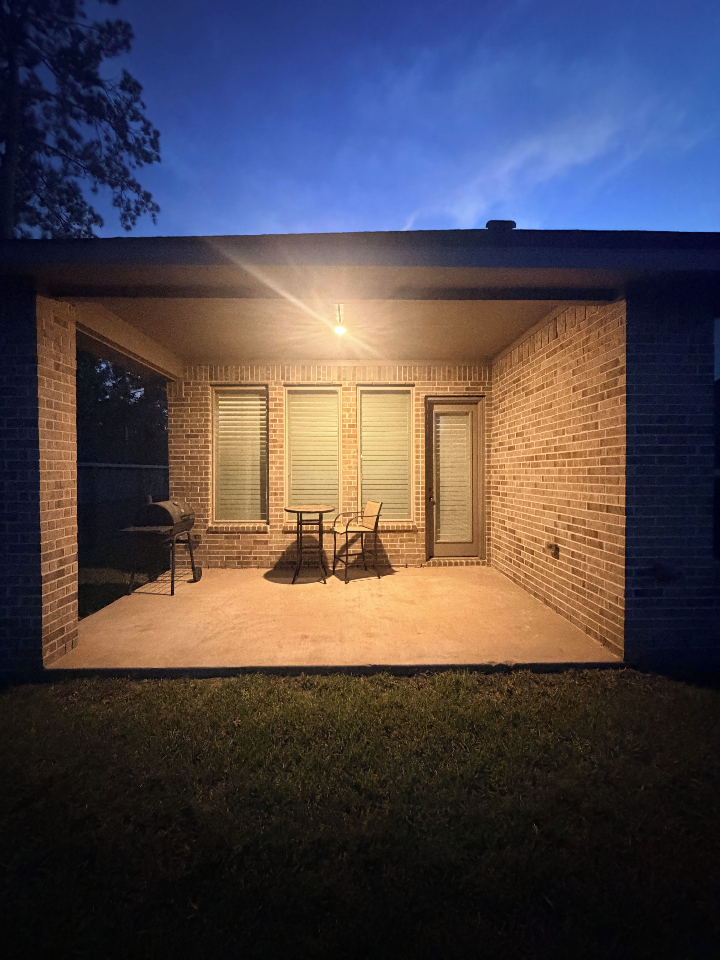 A brick patio with a grill, a table, and chairs.