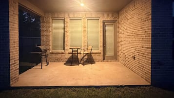 A brick patio with a grill, a table, and chairs.