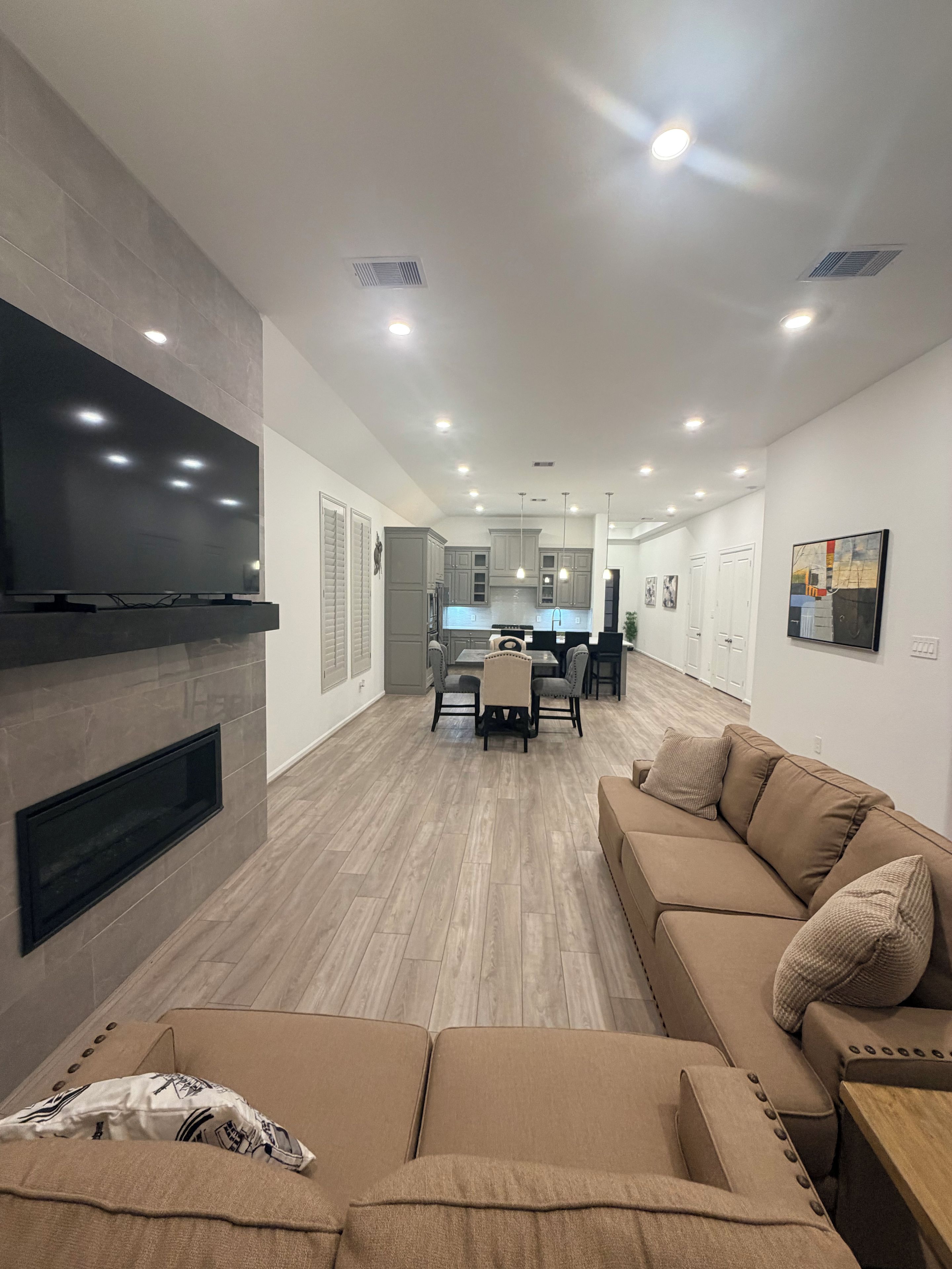 A modern living room with a flat-screen TV, a fireplace, a sofa, and a dining area with a kitchen in the background.