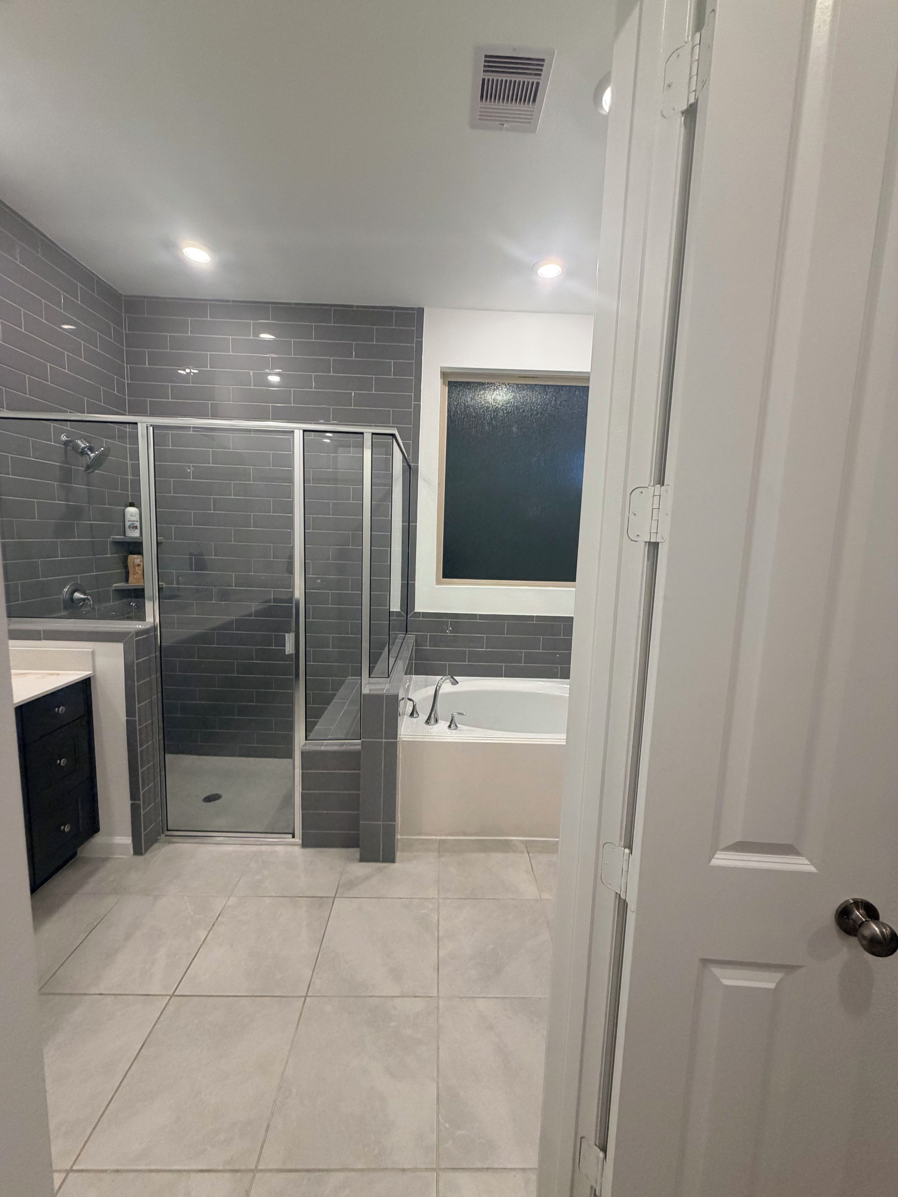 A modern bathroom with a glass shower enclosure, a bathtub, and a window.