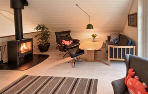 A cozy living room with a wood-burning stove, a dining table, a sofa, a chair, and a potted plant. - Nice home in Gråsten with sauna (Gråsten)