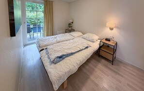 Un dormitori amb un llit, una taula de nit amb una làmpada, un rellotge i una finestra amb cortines.