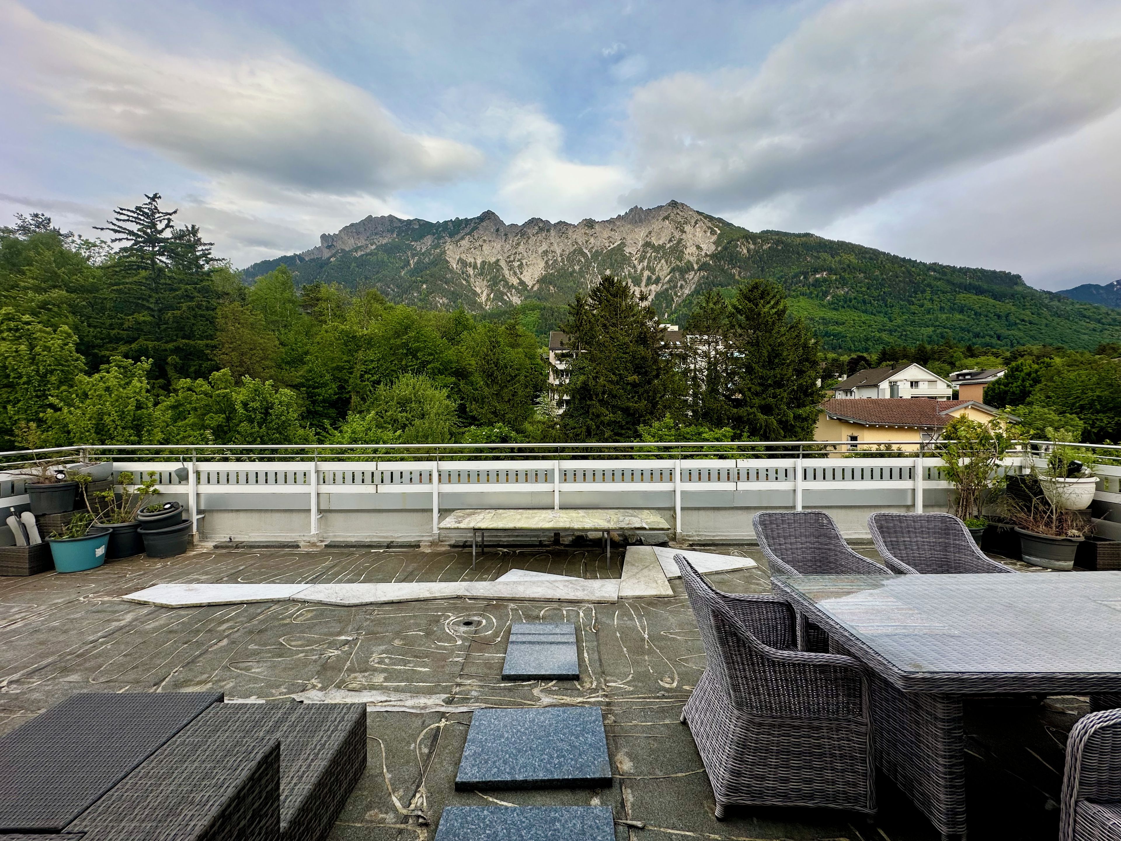 Eine Dachterrasse mit Gartenmöbeln und Topfpflanzen mit Blick auf eine gebirgige Landschaft.
