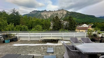 Eine Dachterrasse mit Gartenmöbeln und Topfpflanzen mit Blick auf eine gebirgige Landschaft.