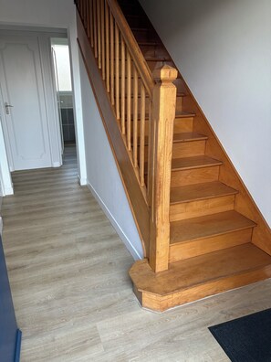 Eine Holztreppe mit Handlauf, die zu einem Raum mit hellem Boden führt.