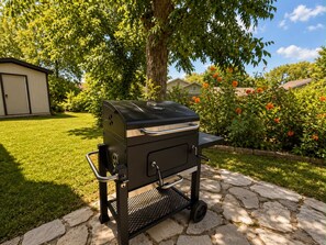 A portable barbecue grill on a stone patio with a lawn and trees in the background. - The Grey Hideaway House - 5 Min to SeaWorld (San Antonio)