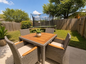 A backyard with a wooden table and wicker chairs, a trampoline, and a covered play area. - The Grey Hideaway House - 5 Min to SeaWorld (San Antonio)