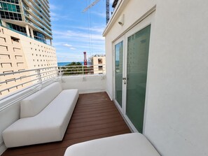 A balcony with a white sofa and a glass door, overlooking a cityscape. - Ocean View South Beach Suite with Double Balconies (Miami Beach)