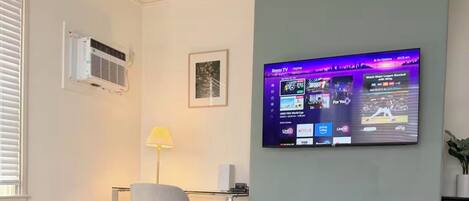 A modern living room with a marble table, a flat-screen TV mounted on the wall, a lamp, and a potted plant.