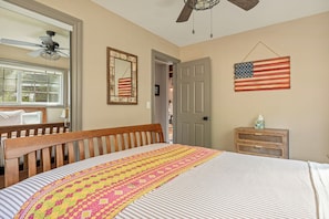 A bedroom with a bed, a wooden headboard, a window, a ceiling fan, a door, and an American flag on the wall. - Lakeview Lodge | Hot Tub + Dock Access + Game Room (Lake Arrowhead)