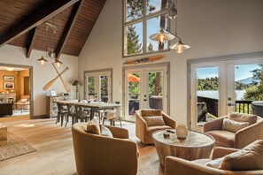 A spacious living area with a high ceiling, large windows, and a dining area with a view of the outdoors. - Lakeview Lodge | Hot Tub + Dock Access + Game Room (Lake Arrowhead)