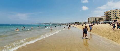 A beach with people, a clear sky, and buildings in the background.