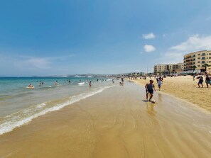 Une plage avec des gens, un ciel dégagé et des bâtiments en arrière-plan.