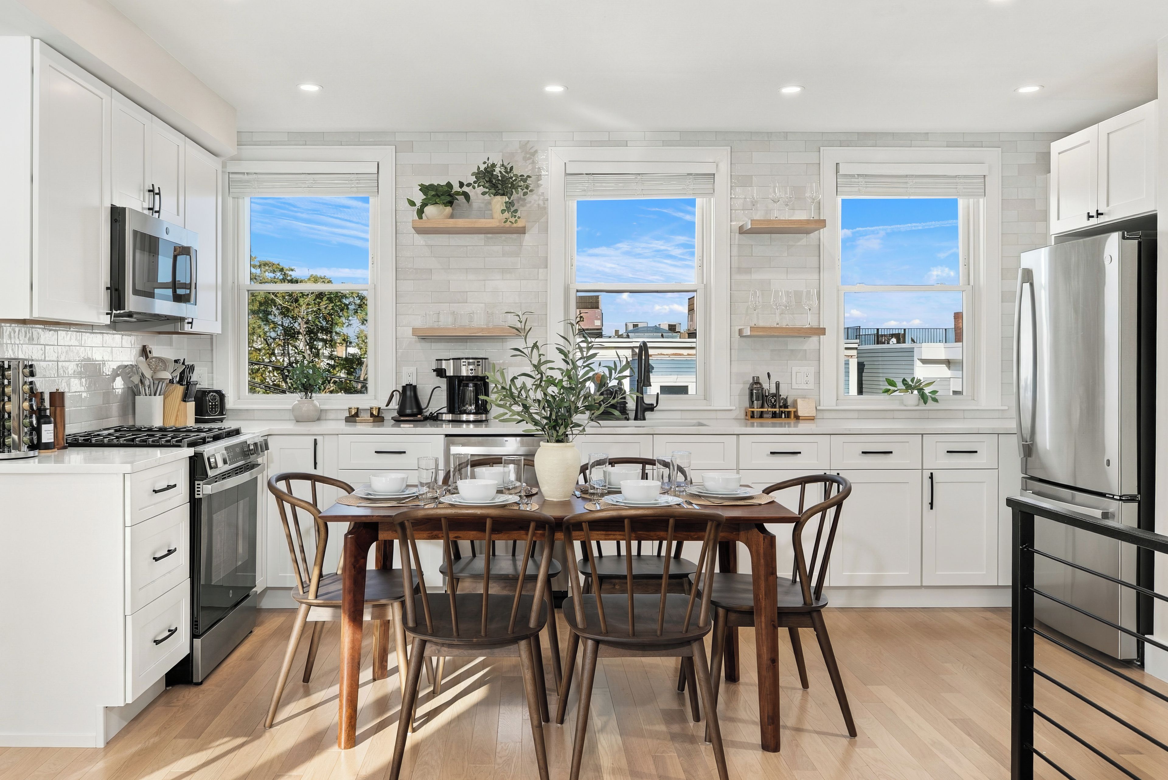 A modern kitchen with white cabinetry, a dining table set for four, and a large window providing a view of the cityscape.