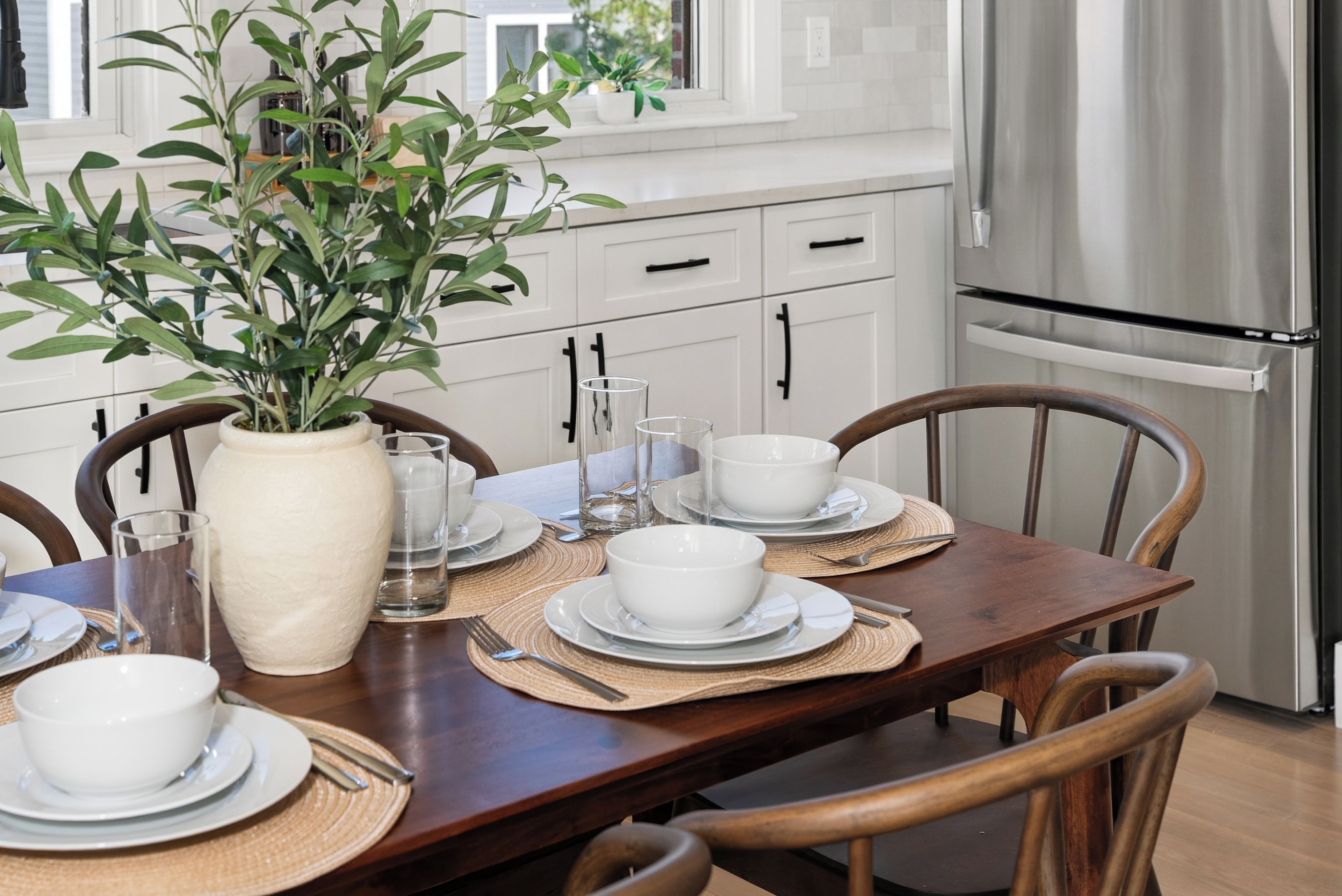 A dining table set with white plates, bowls, and cutlery, surrounded by wooden chairs.