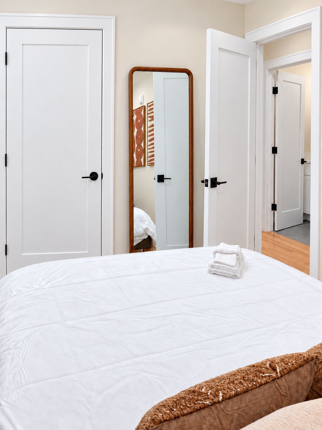 A hotel room with a large bed, a mirror, and a view of another room through an open door.