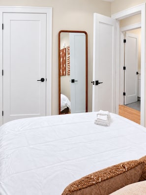 Habitación de hotel con una cama grande, un espejo y vista a otra habitación por una puerta abierta.