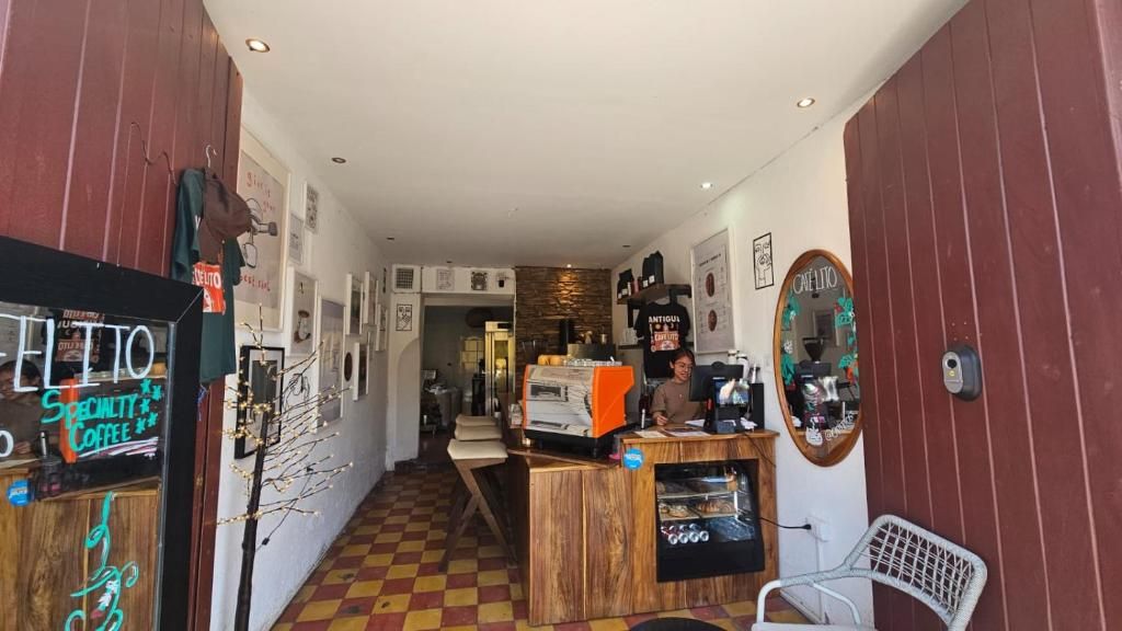 Interior de una cafetería con piso a cuadros, mostrador de madera y un espejo en la pared.