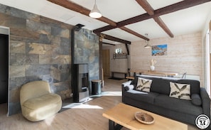 A modern living room with a stone wall, a fireplace, a sofa, and a wooden table. - The Song of the Mountains (BOUTX)