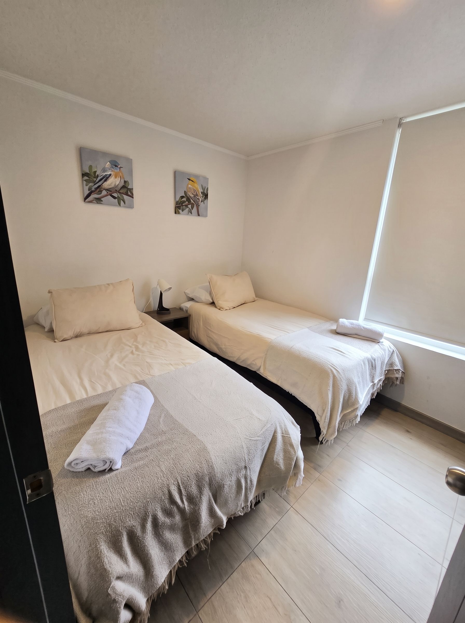 A room with two beds, a nightstand, a lamp, and two wall paintings.