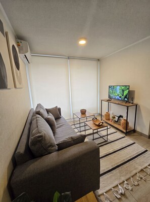 A modern living room with a sectional sofa, a TV on a wooden stand, and a woven rug. - Edificio Rosas by Domus Travels (Santiago)