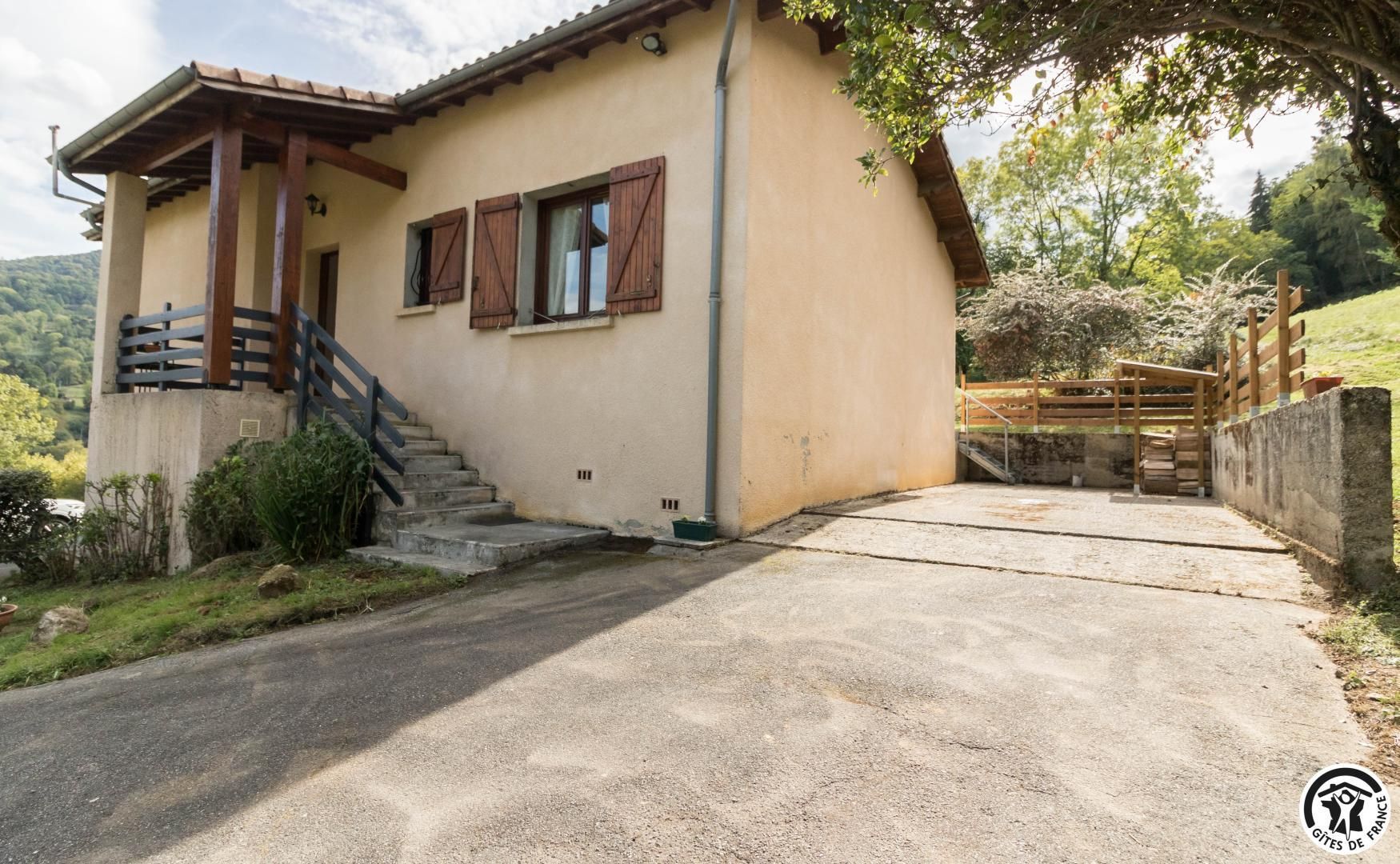 Une maison à deux étages avec un escalier en béton menant à l’entrée, une clôture en bois et une allée pavée.