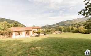 Une propriété rurale comprenant une maison de plain-pied, une cour clôturée et une vue sur des collines ondulantes.