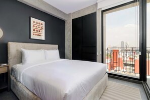 Een moderne hotelkamer met een groot bed, een stadszicht door een schuifdeur en een ingelijste afbeelding aan de muur.