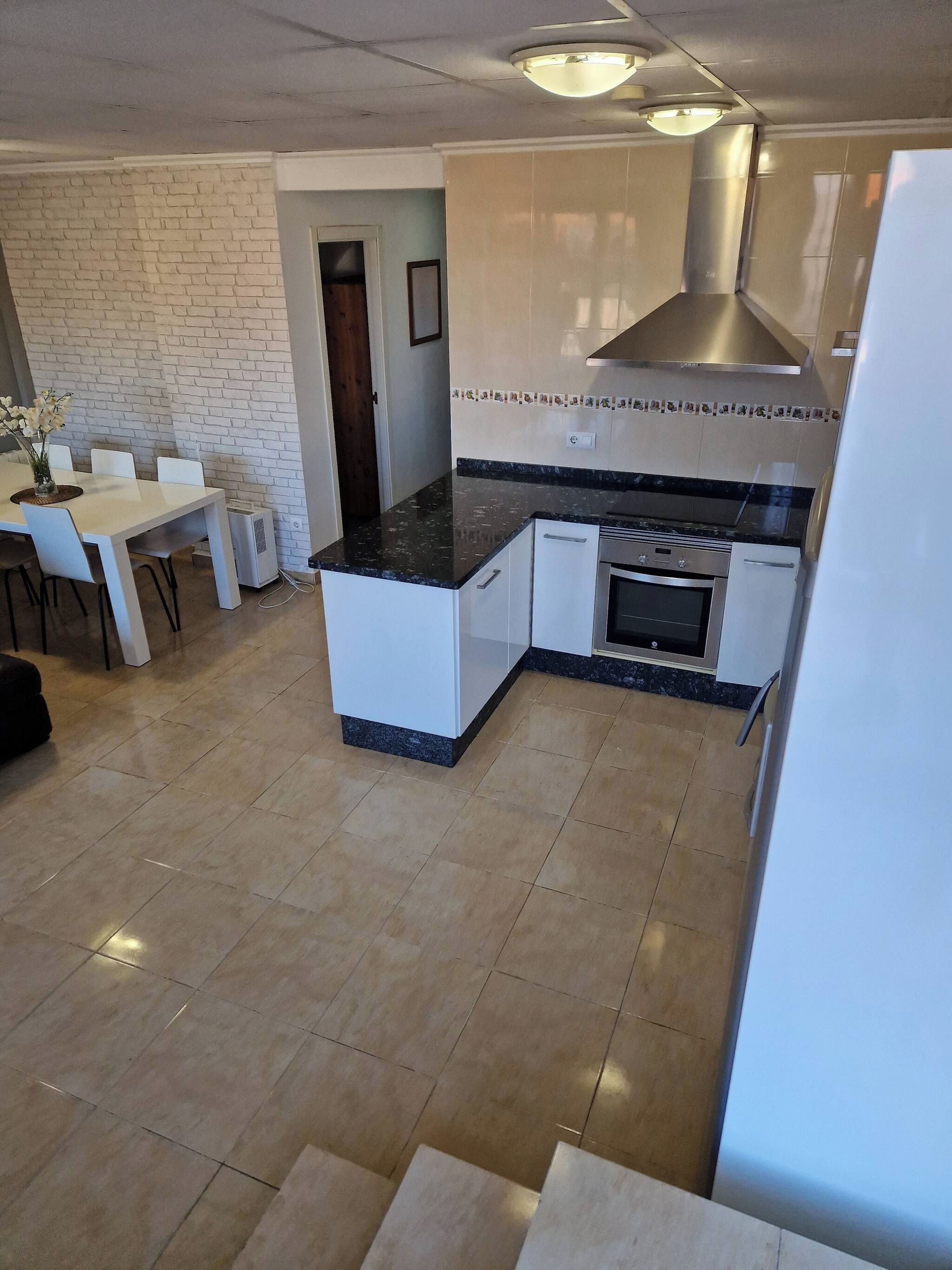 A modern kitchen with a central island, white cabinetry, and a built-in oven.