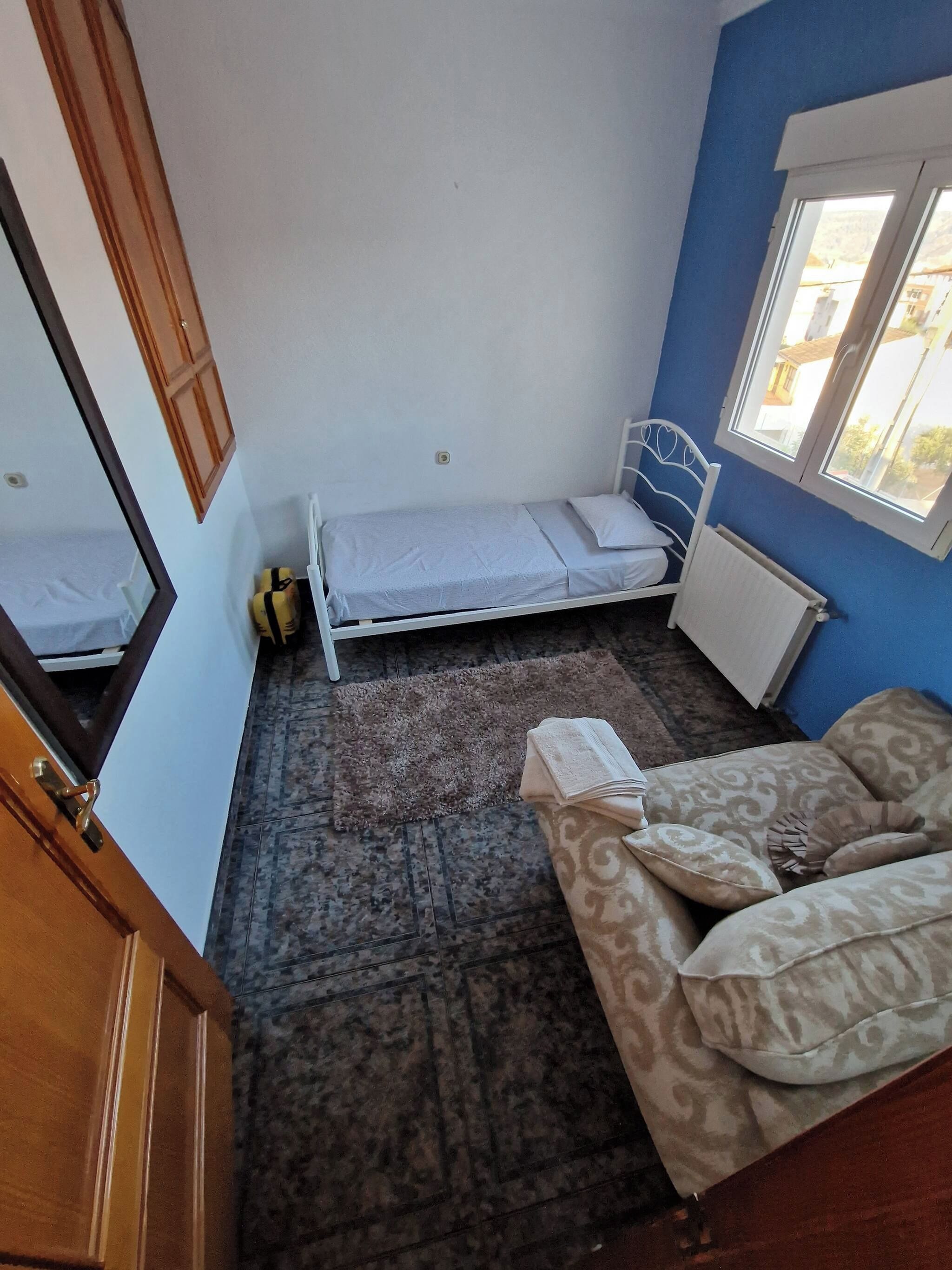 A small room with a single bed, a sofa, a radiator, and a window.