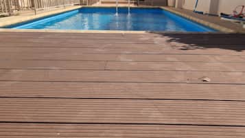 A wooden deck leading to a swimming pool with a view of a building and trees in the background.