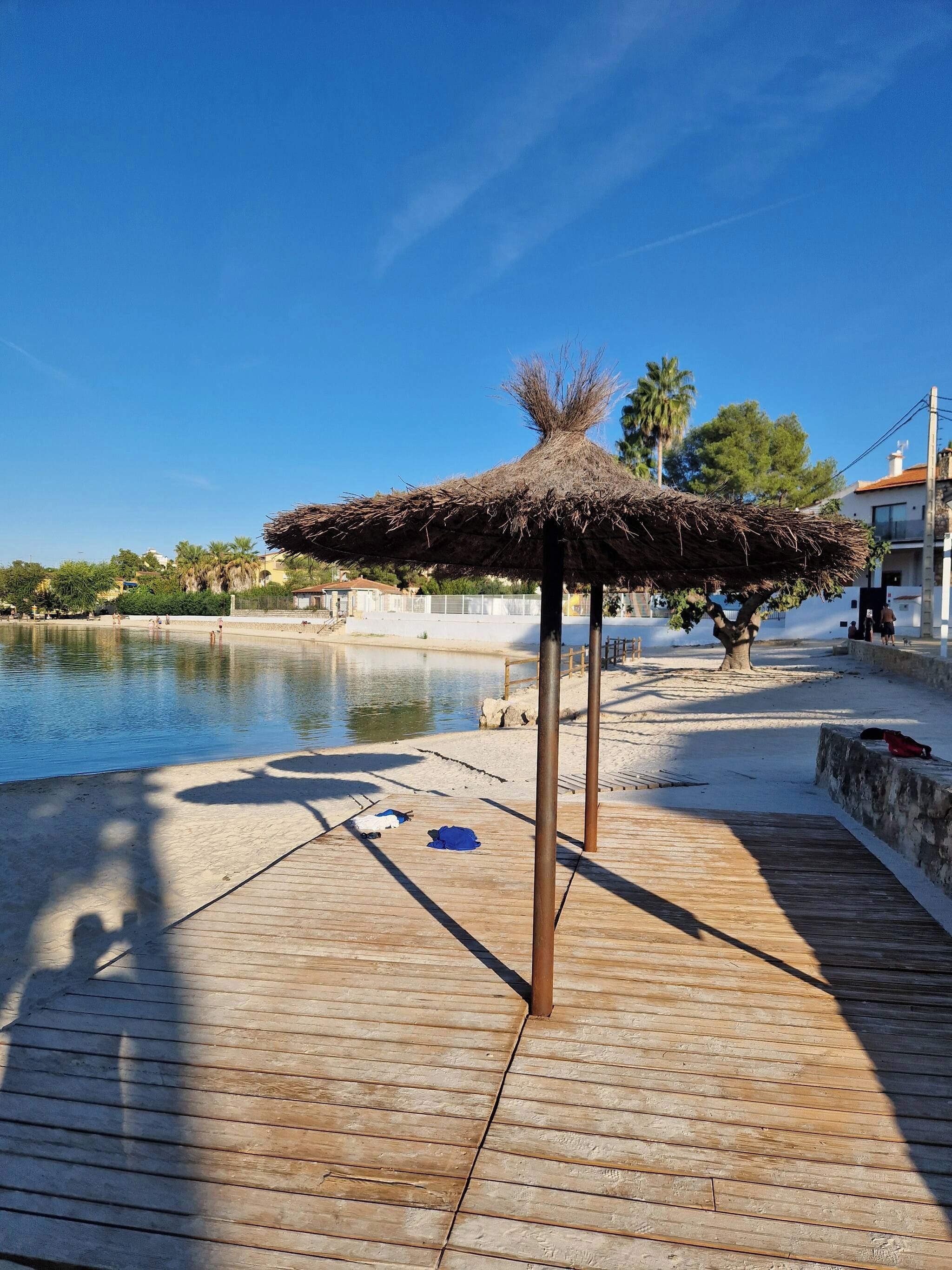 A wooden deck with a thatched structure, a calm water body, and a clear sky.