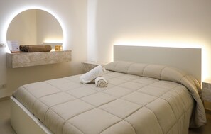 A neatly made bed with a headboard, a towel, and a small table with a candle and a rolled towel. - Stunning apartment in Marina di Ragusa with WiFi (Marina di Ragusa)