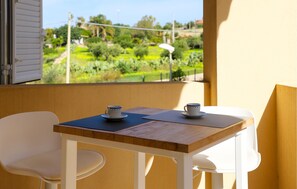 A balcony with a table and two chairs, overlooking a garden with various plants and a pathway. - Stunning apartment in Marina di Ragusa with WiFi (Marina di Ragusa)