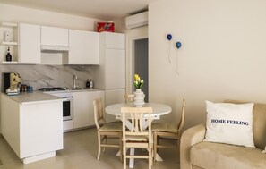 A compact kitchen with white cabinets, a dining table with chairs, and a sofa with a pillow labeled 'HOME FEELING'. - Stunning apartment in Marina di Ragusa with WiFi (Marina di Ragusa)