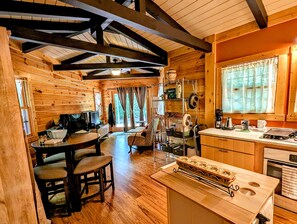Ein gemütliches Blockhaus-Interieur mit einem Essbereich aus Holz, einer Küche und einem großen Fenster mit Vorhängen.