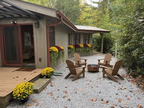 Un espace extérieur aménagé, partiellement abrité, avec des fauteuils Adirondack et un foyer, entouré d’une terrasse en gravier et d’une plateforme en bois.
