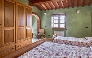 Een kamer met een grote houten garderobe, een enkel bed met een bloemenquilt, een stoel en een raam met uitzicht.