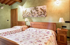 Quarto com duas camas, cabeceiras de madeira, mesas de cabeceira, luminárias e um quadro com flores na parede.