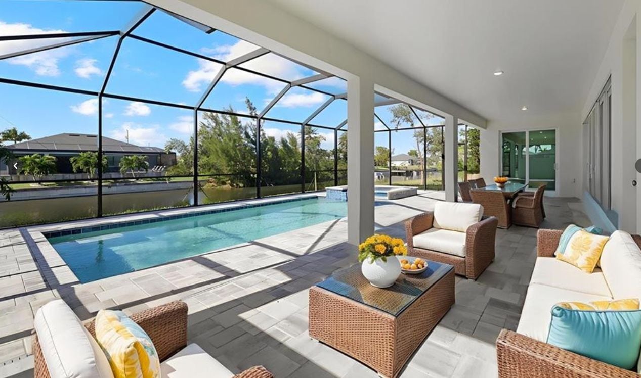 Un espacio exterior cubierto con piscina, mobiliario de mimbre y una mesa de vidrio con flores.