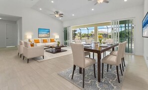 A spacious living room with a dining area, a ceiling fan, and large windows. - Villa Reflection-newly built on water, west facing, pool and spa (Cape Coral)