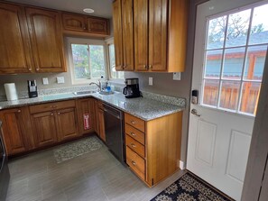 A kitchen with wooden cabinets, a dishwasher, a coffee maker, and a window with a view of a wooden deck. - 3 BED Home w/Hot Tub & Grill (Colorado Springs)