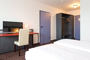 Una habitación de hotel con cama, escritorio, silla, televisor y armario.