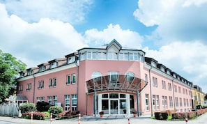 Un hotel de varios pisos con fachada rosa, ventanas amplias y un acceso cubierto.