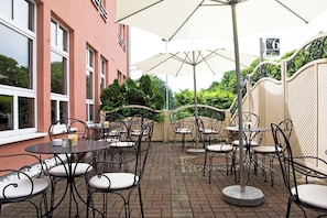 Un patio al aire libre con mesas y sillas, piso de ladrillo y un edificio con ventanas grandes.
