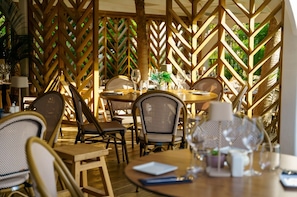 Een buiten eetgedeelte met houten lattenwanden, rieten stoelen en gedekte tafels.