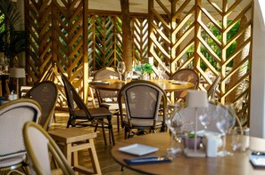 Een buiten eetgedeelte met houten lattenwanden, rieten stoelen en gedekte tafels.