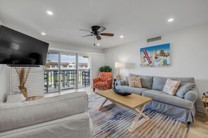 A modern living room with a grey sofa, a wooden coffee table, and a colorful rug. - Chateau by the Sea 30D | Updated Ocean View Condo | Heated Pool | Direct Beach Access (New Smyrna Beach)