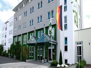Un moderno edificio de hotel con fachada verde y blanca, múltiples ventanas y un asta con una bandera.